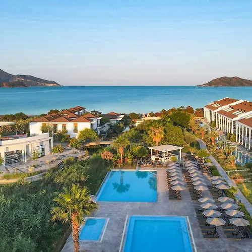Jiva Beach Resort Fethiye Skyline photo Captured from an elevated perspective, this wide shot showcases a luxurious resort nestled along a stunning coastline. The scene is bathed in the soft light of either early morning or late afternoon, with a clear blue sky dominating the upper portion